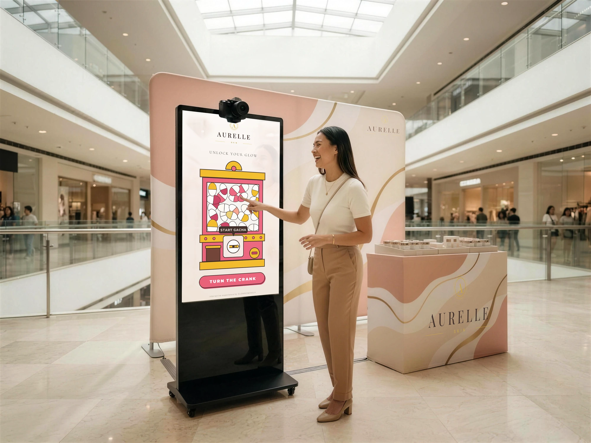 A guest using a branded digital gacha game on SlowMoManila's tall touchscreen kiosk at a mall atrium activation, beside a matching product counter.